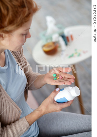 Sick woman suffering from flu holding pills on palm Sick woman suffering from flu holding pills on palm 58555231