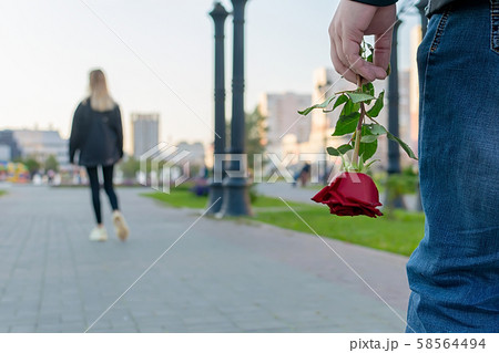 red rose flower in the hand of the guy on the background of the girl leaving him 58564494