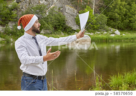 Young man with a beard in a Santa Claus hat with a Young man with a beard in a Santa Claus hat with a 58570650