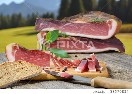 Typical South Tyrolean bacon snack with rye bread lying in front of alpine pastures of the alps 58570834