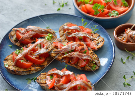 Spanish bar food: Grilled slices of bread with olive oil, herbs, fresh tomatoes and anchovy fillets 58571743