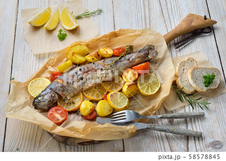 Baked lemon trout with oven-roasted rosemary potatoes and tomatoes, served on baking paper Baked lemon trout with oven-roasted rosemary potatoes and tomatoes, served on baking paper 58578845