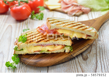 Grilled and pressed toast with smoked ham, cheese, tomato and lettuce served on a wooden table 58579352