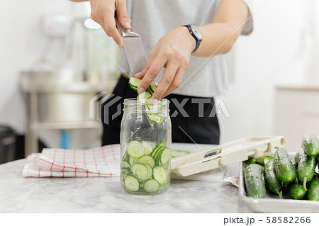Woman hands with knife putting cucumber into glass jar in kitchen table. Woman hands with knife putting cucumber into glass jar in kitchen table. 58582266
