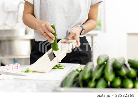Woman slicing cucumber with vegetable slicer for salad. Woman slicing cucumber with vegetable slicer for salad. 58582269