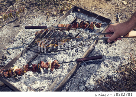 Caucasian man cooking skewered meat and fish over charcoal Caucasian man cooking skewered meat and fish over charcoal 58582781