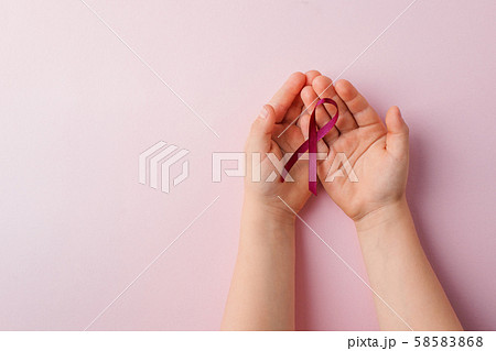Concept for fear, domestic violence and family or child abuse. Purple ribbon symbol in kids hands on pink background Concept for fear, domestic violence and family or child abuse. Purple ribbon symbol in kids hands on pink background 58583868