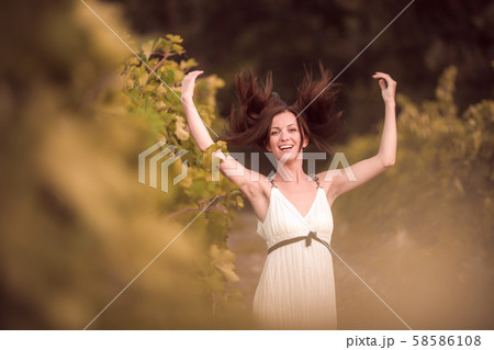 Smiling woman in white dress standing in vineyard 58586108