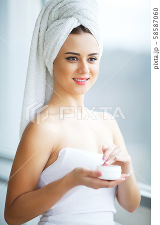Young woman standing in bathroom and applying face cream in the morning 58587060