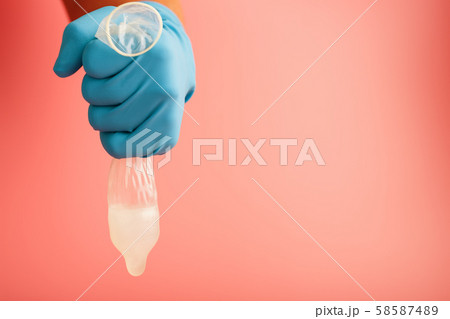 A condom that missed a drop of sperm. A hand in a blue glove holds a used contraceptive on a red A condom that missed a drop of sperm. A hand in a blue glove holds a used contraceptive on a red 58587489