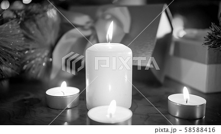 Closeup black and white image of burning candles aginst Christmas gifts and presents 58588416
