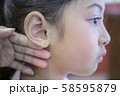 Adorable little Asian girl having ear piercing process. 58595879