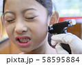 Adorable little Asian girl having ear piercing process. 58595884