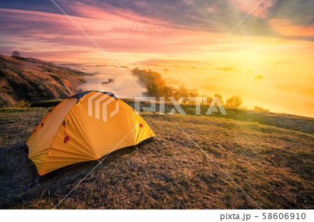 Orange tent on hill above foggy river under bright sun 58606910