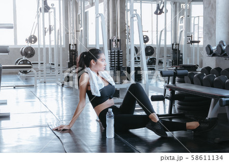Fit young woman sitting on gym floor for relaxing Fit young woman sitting on gym floor for relaxing 58611134