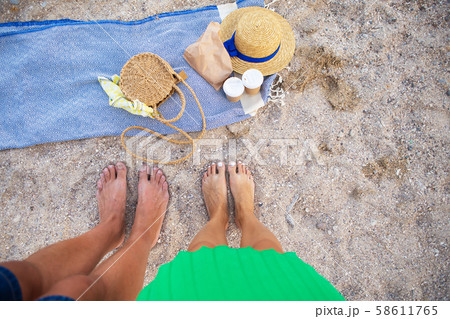 Picnic near the sea. A blue plaid on which are glasses with coffee, a bag, a hat. Feet of a couple 58611765