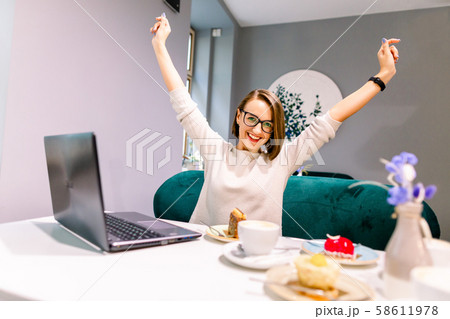 Portrait of beautiful smiling woman in glasses in winning pose sitting in a cafe with laptop indoors Portrait of beautiful smiling woman in glasses in winning pose sitting in a cafe with laptop indoors 58611978