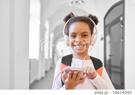 Schoolgirl with headphones standing in hallway, smiling. Schoolgirl with headphones standing in hallway, smiling. 58614090