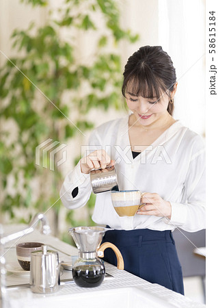 陶器のコーヒーカップに注いだエスプレッソにクリーム状に泡立てたミルクを加えたカプチーノを淹れる女性 陶器のコーヒーカップに注いだエスプレッソにクリーム状に泡立てたミルクを加えたカプチーノを淹れる女性 58615184