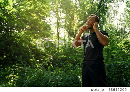 Runner standing and listening music in forest. 58615206