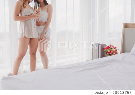 Women in pajamas drinking champagne close curtains 58618767