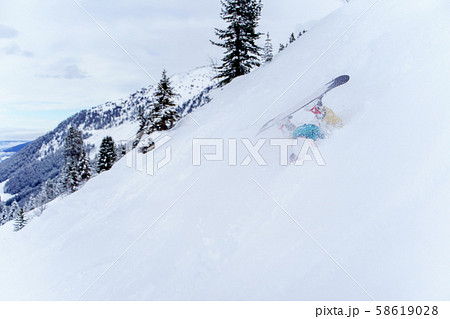 Photo of sporting man riding snowboard on snowy slope , legs sticking up 58619028