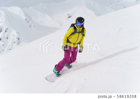Woman in helmet and mask is riding on snowboard on snowy slope at winter day. Woman in helmet and mask is riding on snowboard on snowy slope at winter day. 58619208