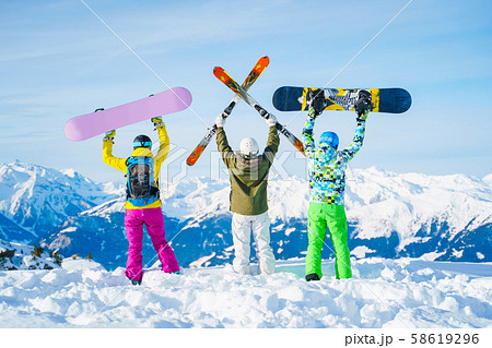 Photo from behind of three athletes with arms raised with snowboards and skis on day . Photo from behind of three athletes with arms raised with snowboards and skis on day . 58619296