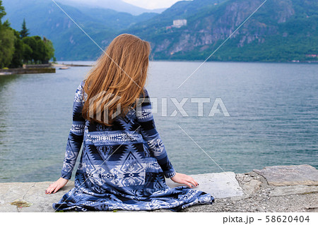 Back view of girl sitting near lake Como, mountain in background. 58620404