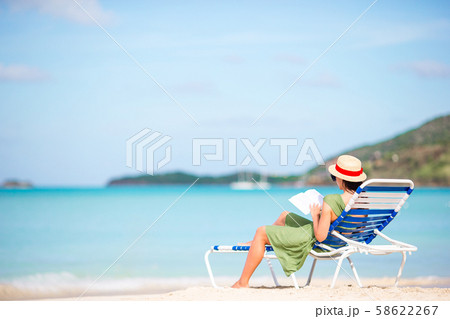 Young woman reading book on chaise-lounge on the beach Young woman reading book on chaise-lounge on the beach 58622267