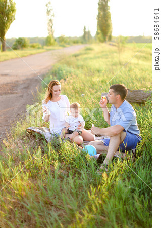 Gladden parents sitting on grass with little child and blowing bubbles. Gladden parents sitting on grass with little child and blowing bubbles. 58634641