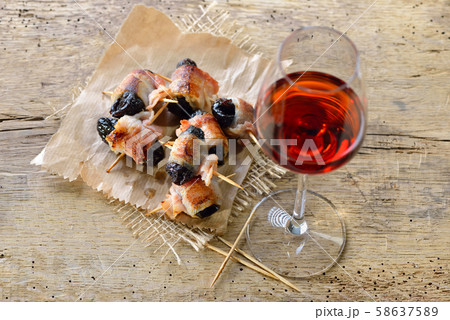 Delicious Spanish tapas: Fried prunes wrapped in bacon with a glass of red wine 58637589
