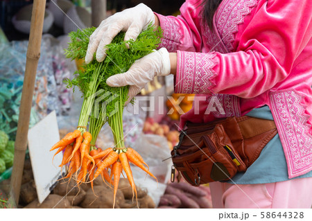 Female hands with white gloves holding bunch of carrots in farmers market. 58644328