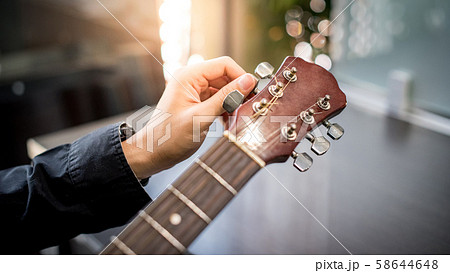 Male hand adjusting pegs on acoustic guitar 58644648