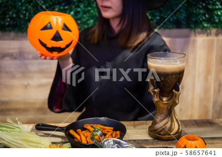 Beautiful young surprised woman or Halloween Witch dark style with holding a pumpkin and black drink in Halloween celebrate night party. Copy space background and soft or select focus 58657641