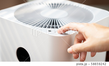 Closeup hand of a woman press the power button of an air purifier machine to turn it on when dust air pollution situation outside is harmful and unhealthy base on air quality index. PM 2.5, Polluted. 58659242