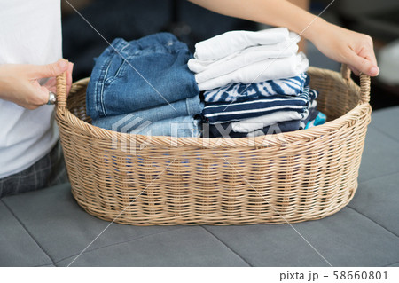 Woman's hands carrying a bamboo laundry basket with clean and folded kids clothes, t-shirt, jeans, inside. Laundry, House work, Mom daily routine, Chores concept. 58660801