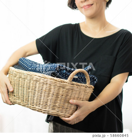 A happy housewife's carrying a weaving bamboo laundry basket full of clean and soft towel folded neatly inside. Laundry, Household, Detergent, Softener, Chores, Mommy daily routine concept. 58660845