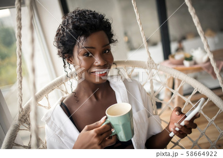 Beaming woman drinking cappuccino and using smartphone Beaming woman drinking cappuccino and using smartphone 58664922