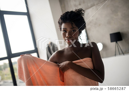 Curly dark-eyed woman covering body in towel after having bath Curly dark-eyed woman covering body in towel after having bath 58665287