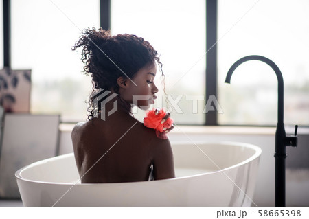 Curly dark-skinned woman holding loofah while having bath 58665398