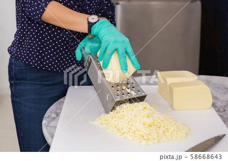 Woman with green gloves grating cheese on kitchen table. 58668643
