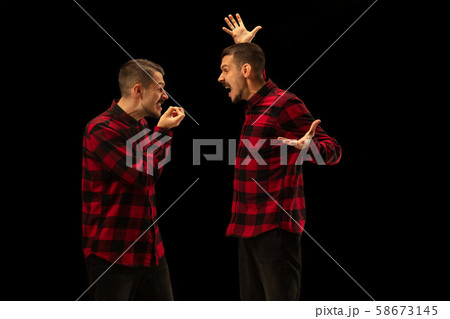 Young handsome man arguing with himself on black studio background. Young handsome man arguing with himself on black studio background. 58673145