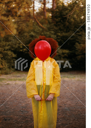 Woman in a yellow raincoat holding a red balloon on the background of forest. 58674950