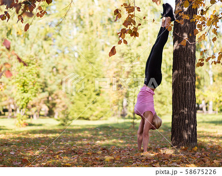 Athletic woman make a classic handstand by the tree outdoor in urban park in autumn, selective focus Athletic woman make a classic handstand by the tree outdoor in urban park in autumn, selective focus 58675226