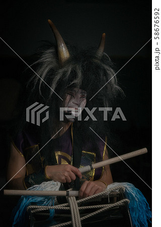 Taiko drummer in a wig and a demon mask sitting 58676592