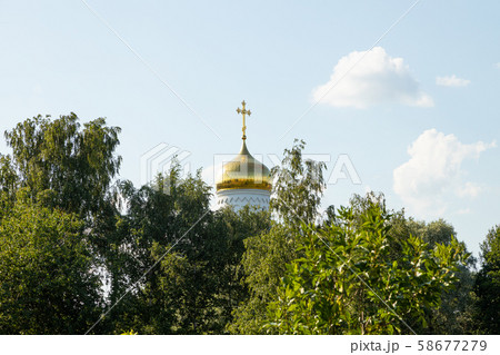 Gilt dome of white Orthodox church surrounded by green tops of trees Gilt dome of white Orthodox church surrounded by green tops of trees 58677279