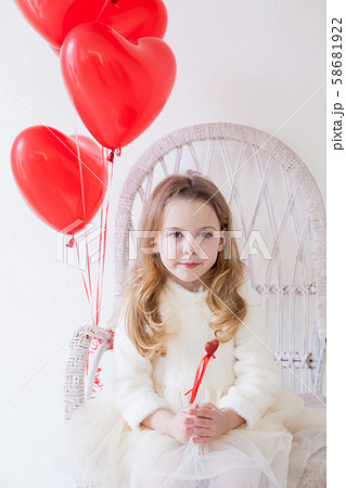 Girl sits on a chair in a room with red holiday balloons 58681922