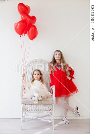 Two girls sit on a chair with red holiday balloons Two girls sit on a chair with red holiday balloons 58681935