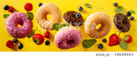 Various decorated doughnuts with sprinkles and berries in motion falling on yelloy background Various decorated doughnuts with sprinkles and berries in motion falling on yelloy background 58686664